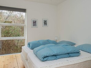 A bedroom with a large window, a bed with blue bedding, and two framed pictures on the wall.