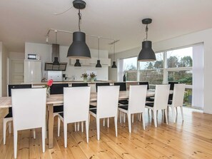 A modern kitchen with white cabinets, a wooden dining table, and black pendant lights.