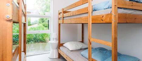 A bunk bed room with a window, a bedside table, and a view of greenery outside.