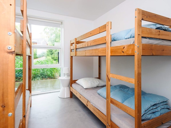 A bunk bed room with a window, a bedside table, and a view of greenery outside.