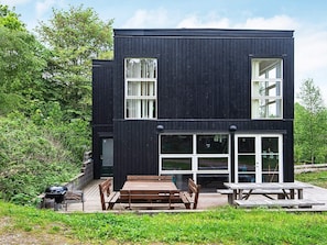 Ein modernes, zweistöckiges Gebäude mit schwarzer Fassade, großen Fenstern und einer Holzterrasse mit Bänken.