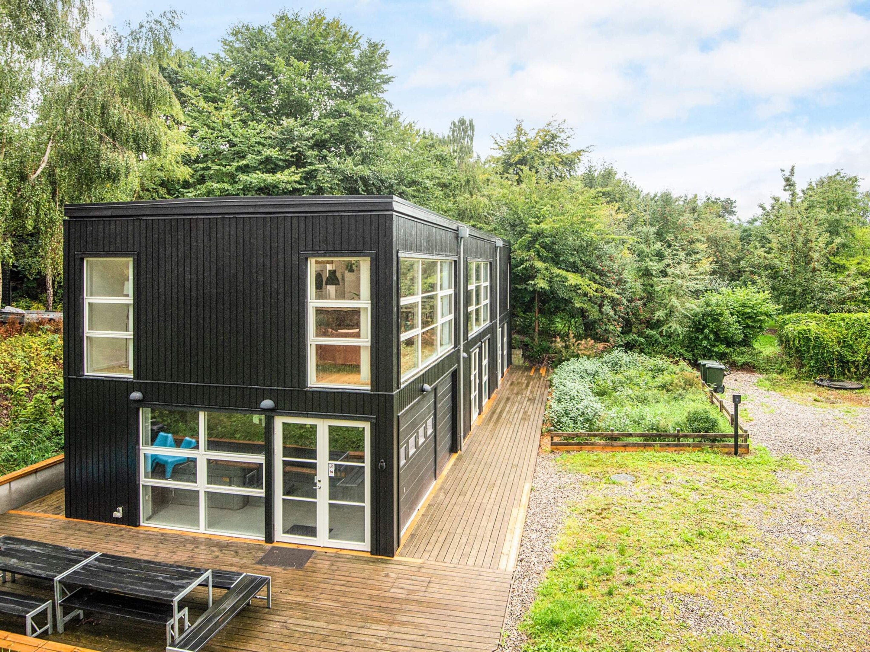 A modern black building with multiple windows, a wooden deck, and a garden area.