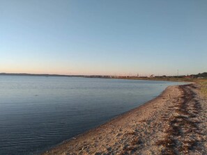 A calm body of water with a sandy shore and distant buildings.