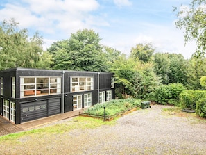 A modern two-story building with large windows and a garage, surrounded by a gravel driveway and lush greenery. - Gorgeous Holiday Home in Ebeltoft with Hot Tub (Ebeltoft)