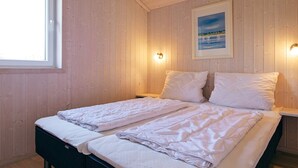 A double bed with white linens in a room with wooden walls and a framed picture on the wall.