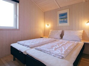 Un lit double avec du linge de lit blanc, dans une pièce aux murs en bois et ornée d’un tableau encadré.