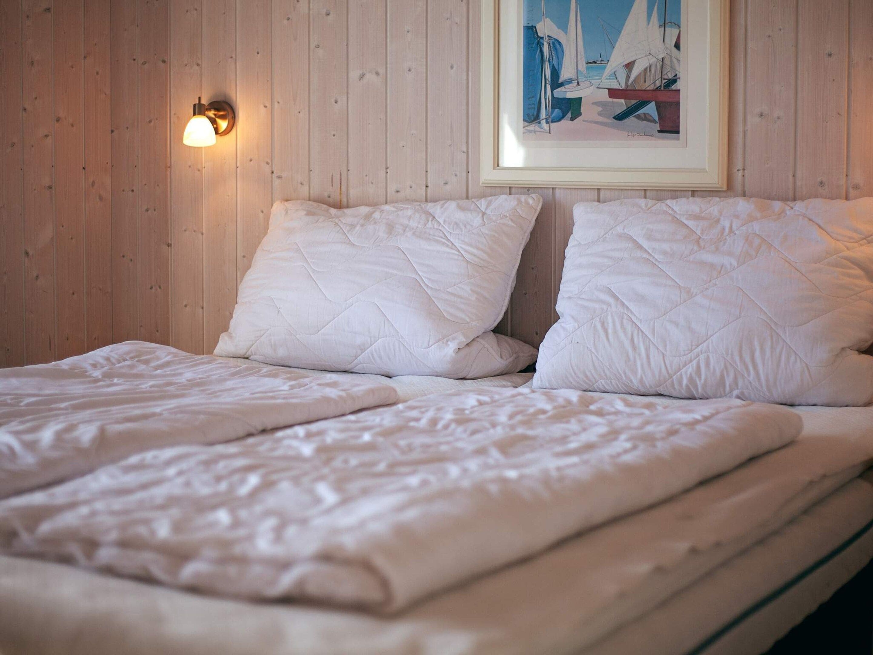 A bed with white bedding and a wall-mounted light fixture.