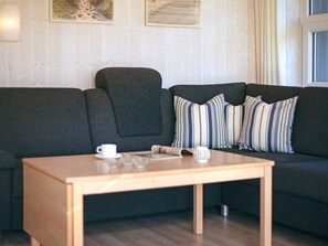 A modern living room with a dark grey sofa, striped pillows, a wooden coffee table, and a white cup.