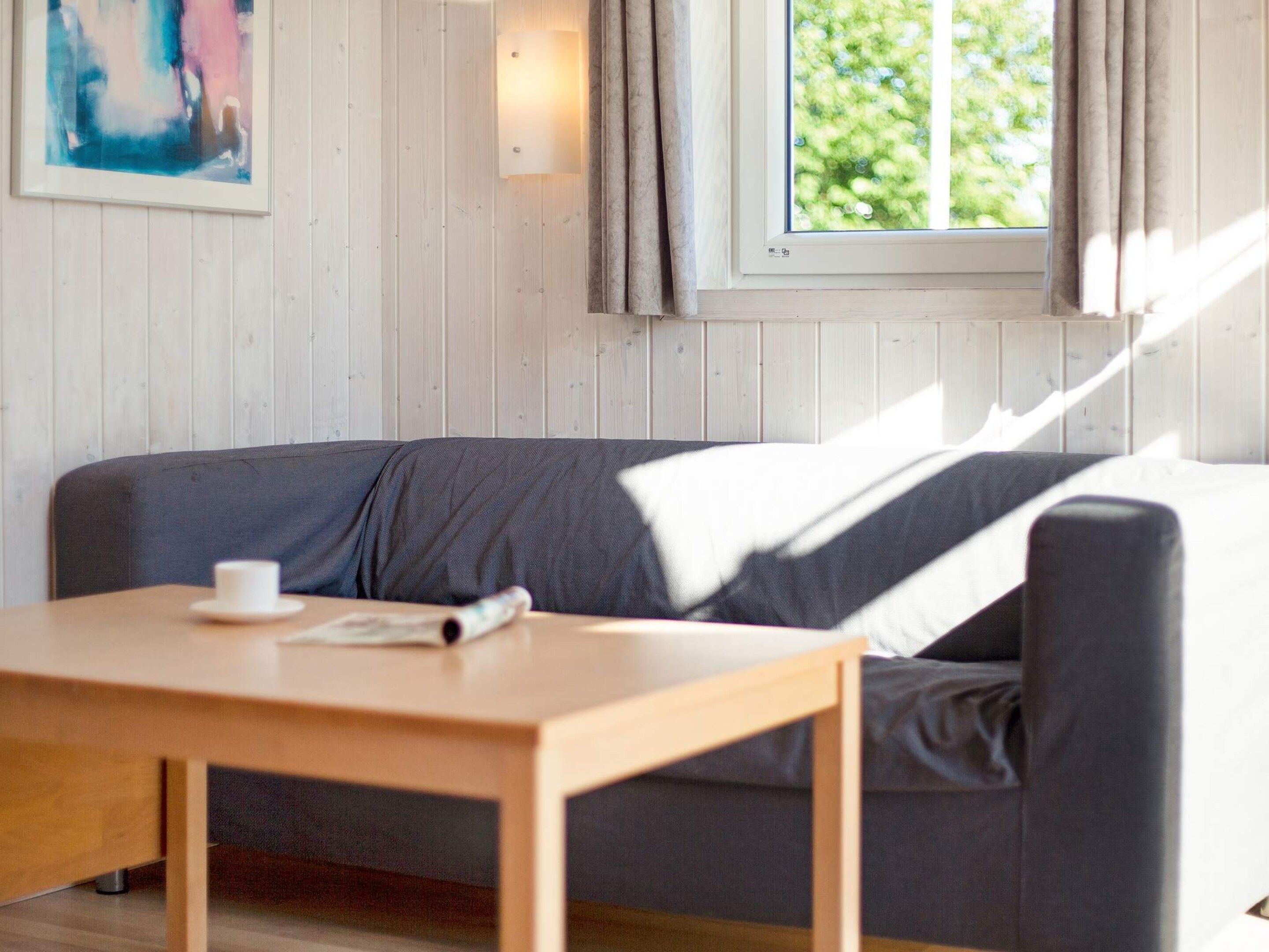 Une pièce avec une table en bois, un canapé gris et une fenêtre avec des rideaux.