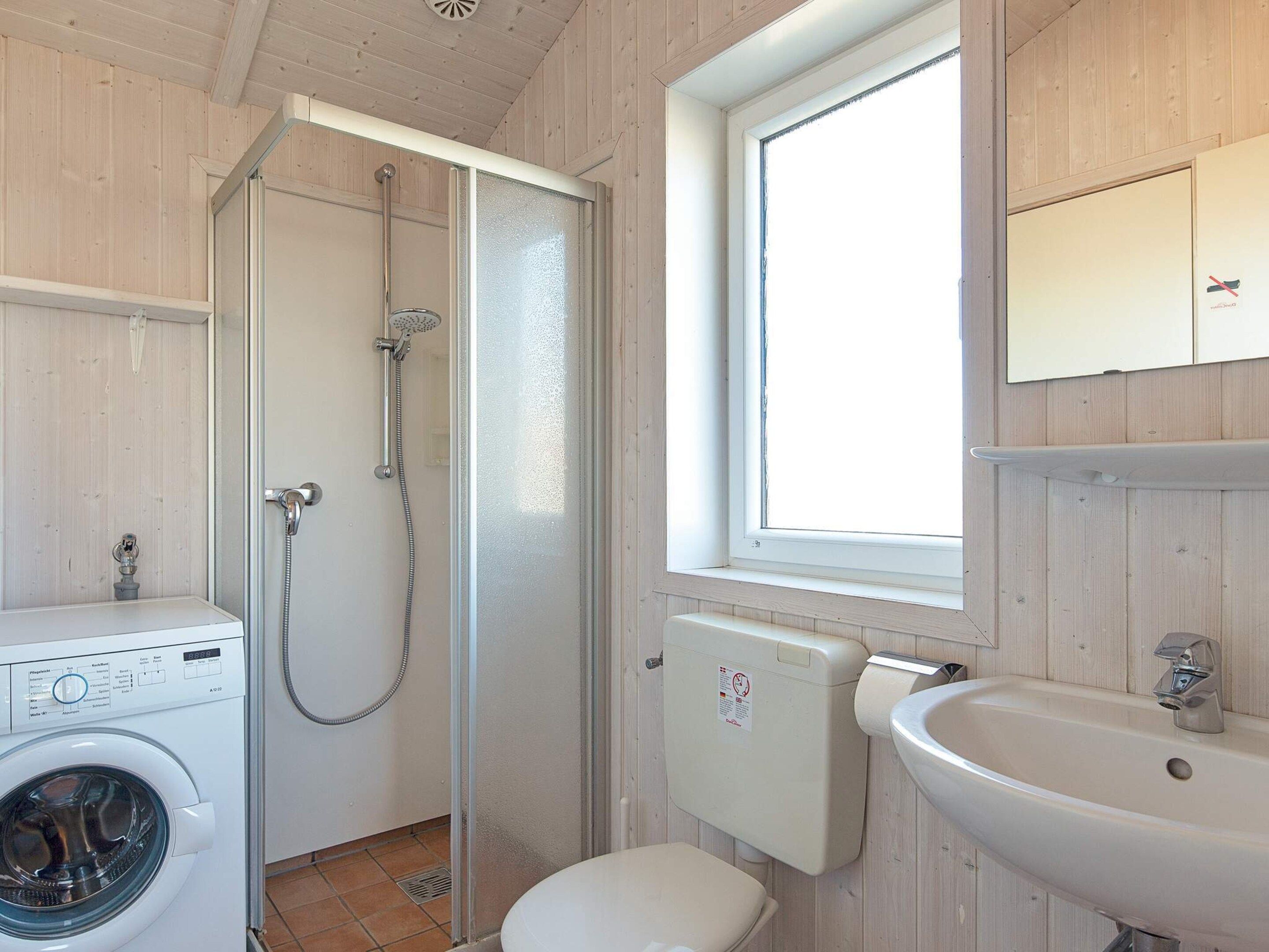 Une salle de bain compacte comprenant un lave-linge, un espace douche, des toilettes et un lavabo.