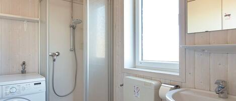 Une salle de bain compacte comprenant un lave-linge, un espace douche, des toilettes et un lavabo.