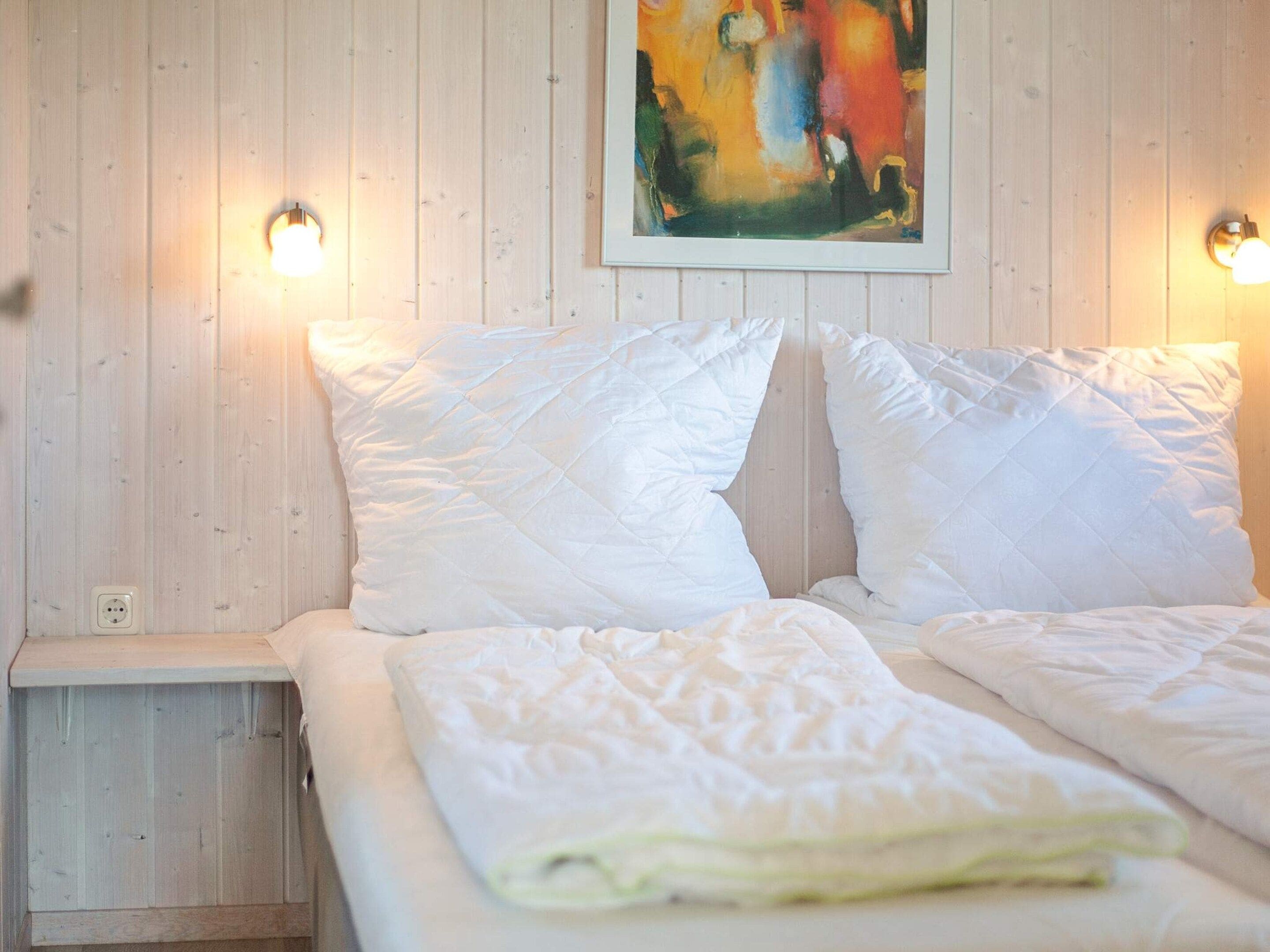 Una cama con ropa de cama blanca y dos lámparas fijadas a la pared.