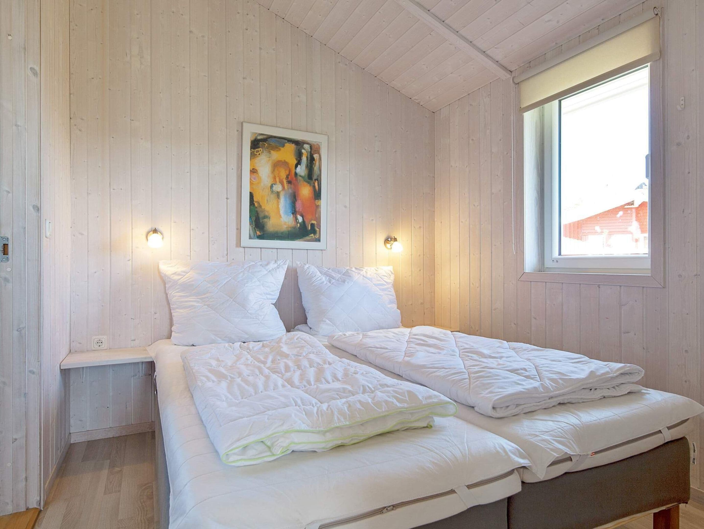 A bedroom with a wooden ceiling, a bed with white bedding, a painting on the wall, and a window with a view of a building outside.
