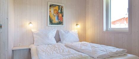 A bedroom with a wooden ceiling, a bed with white bedding, a painting on the wall, and a window with a view of a building outside.