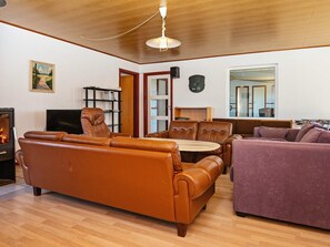 A living room with a sofa, a loveseat, a dining table, a TV, a fireplace, and a bookshelf. - 10 Person Holiday Home in Harboore (Harboore)