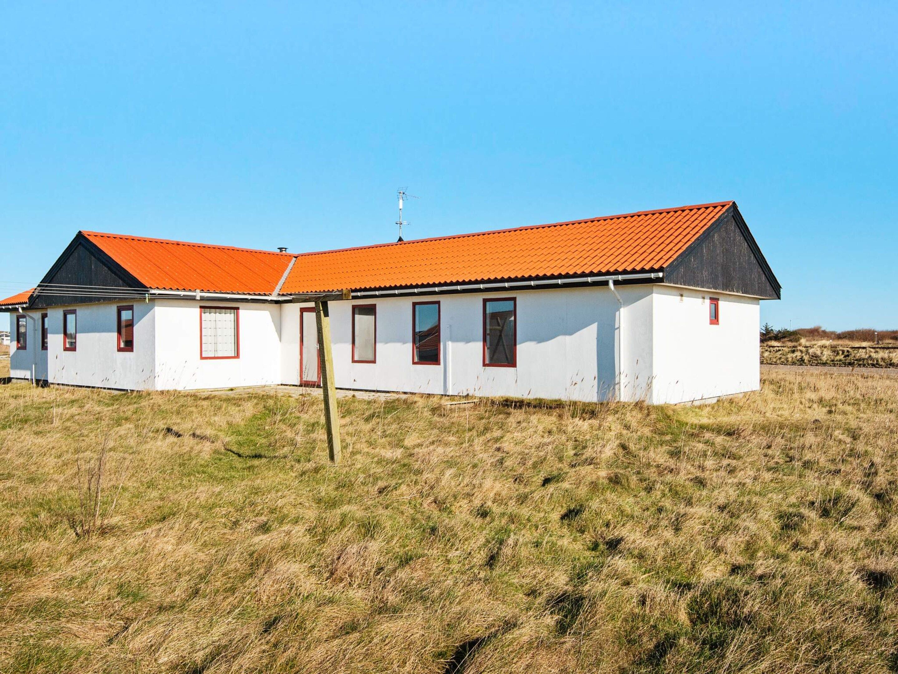A two-story building with a red-tiled roof and white walls, located in a grassy field.