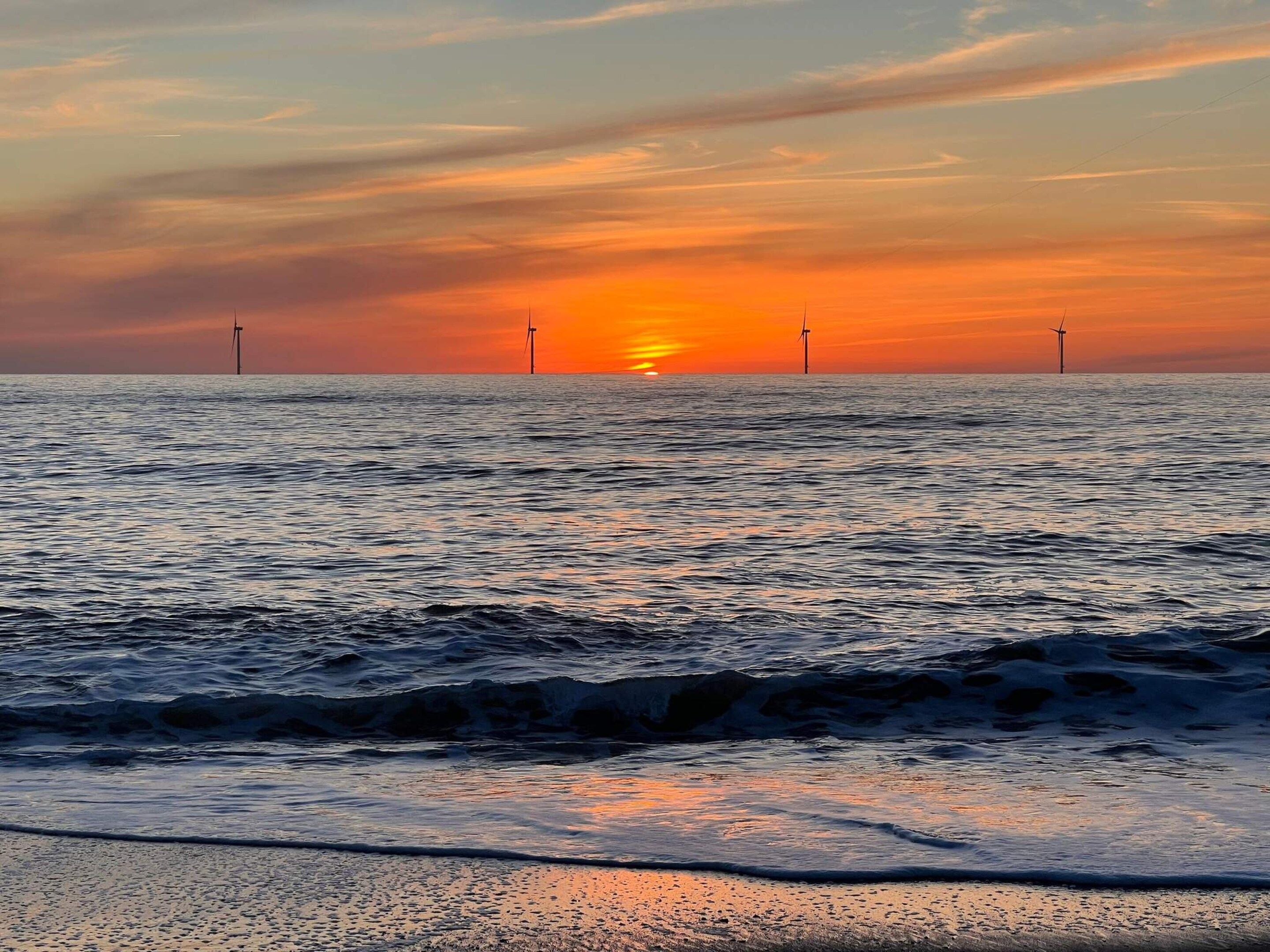 A sunset over the ocean with wind turbines in the distance.