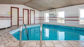 Una piscina interior con agua cristalina, rodeada de paredes con azulejos y un techo de madera.