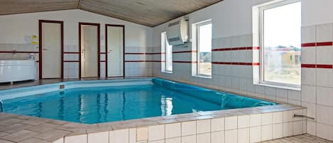An indoor swimming pool with tiled walls, a wooden ceiling, and a window providing a view outside.