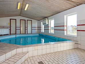 Piscina interna com paredes azulejadas, teto de madeira e janela com vista externa.
