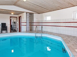 An indoor swimming pool with a wooden ceiling, tiled walls, and a clear view of the pool area.