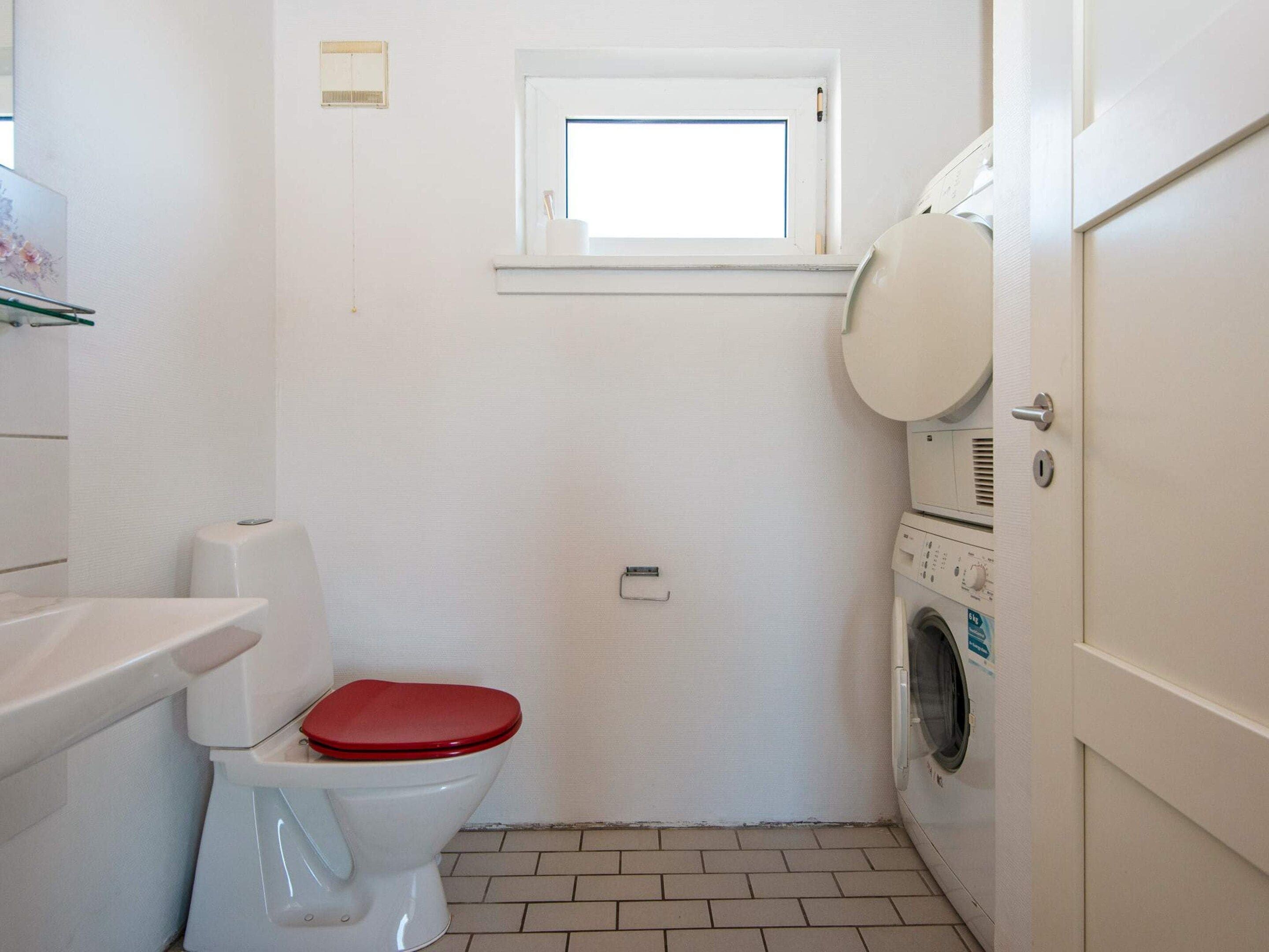 A compact bathroom with a toilet, a washing machine, and a small window.
