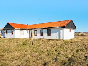 A white building with a red roof and black trim, situated in a grassy field. - 10 Person Holiday Home in Harboore (Harboore)
