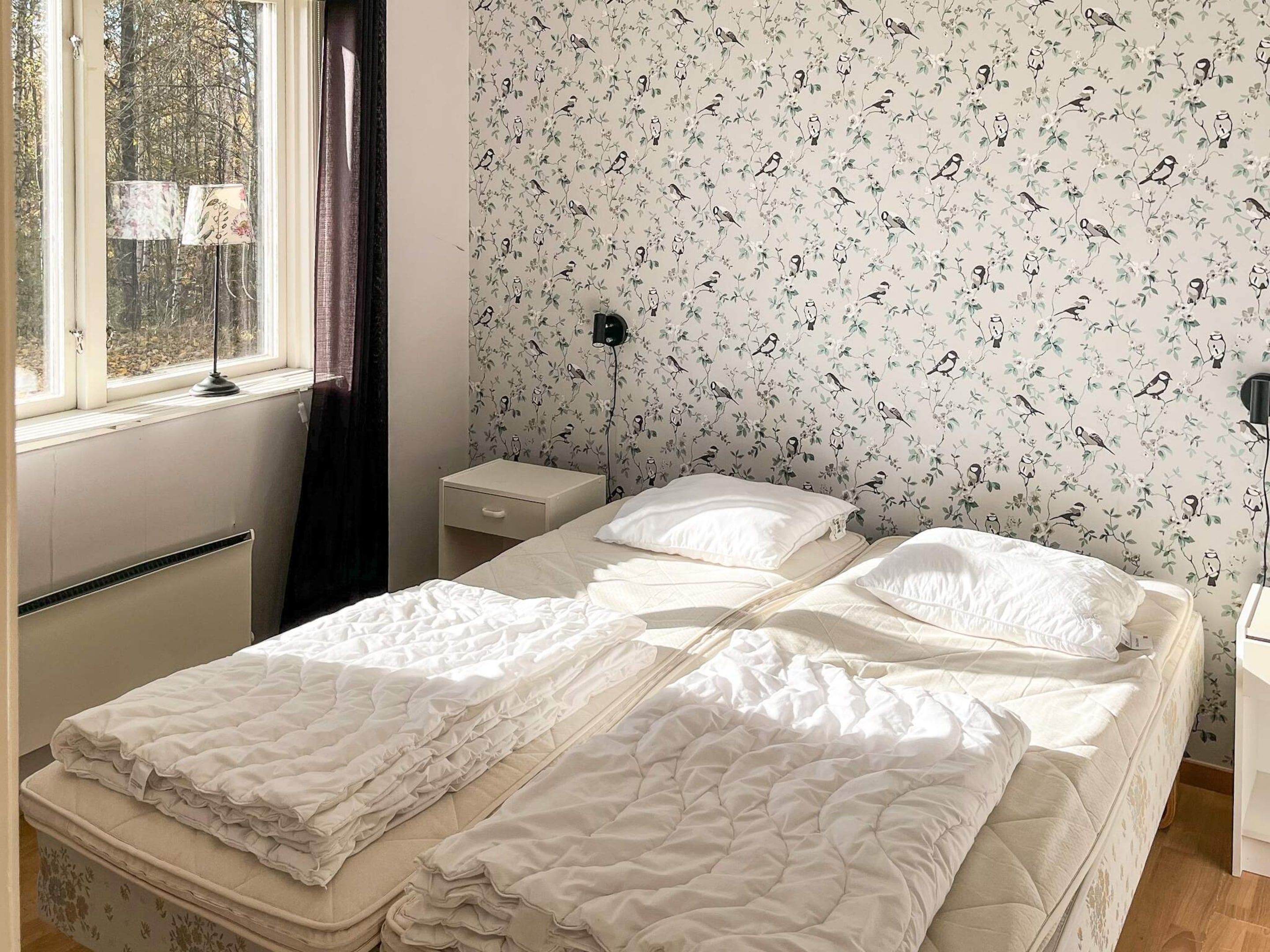A bedroom with a bed, a nightstand, a lamp, and a window with curtains.