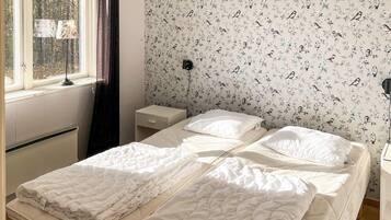 A bedroom with a bed, a nightstand, a lamp, and a window with curtains.