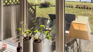 A view from a window overlooking a grassy area with a wooden deck, outdoor furniture, and a lake. - Holiday Home in HÃ¥cksvik (Håcksvik)