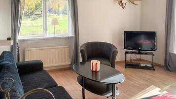 Ett vardagsrum med en soffa, ett bord med ett ljus, en tv på ett tv-bord och ett fönster med gardiner.