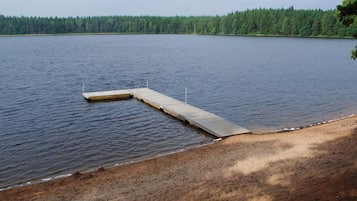 En stilla sjö med en träbrygga som sträcker sig ut i vattnet, omgiven av en skogbeklädd strand.