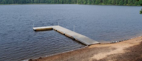A calm lake with a wooden dock extending into the water, surrounded by a forested shoreline.