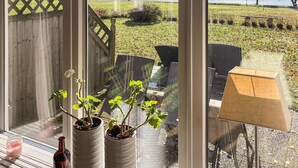 A view from a window overlooking a lake, with outdoor furniture and potted plants on a patio. - Holiday Home in HÃ¥cksvik (Håcksvik)