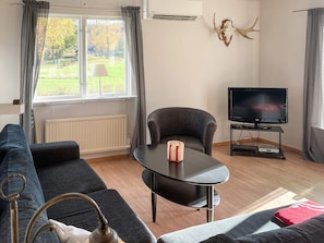 A living room with a sofa, a table with a candle, a TV on a stand, and a window with curtains.