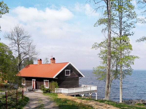 A wooden cabin with a red roof, a porch, and a view of the water.