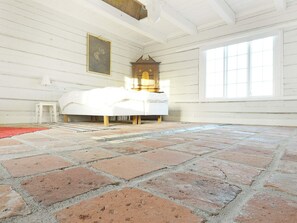 A room with a brick floor, a white bed, a wooden cabinet, and a window.