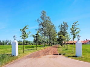 A rural road leading to a building with a red roof, flanked by white lamp posts and trees.