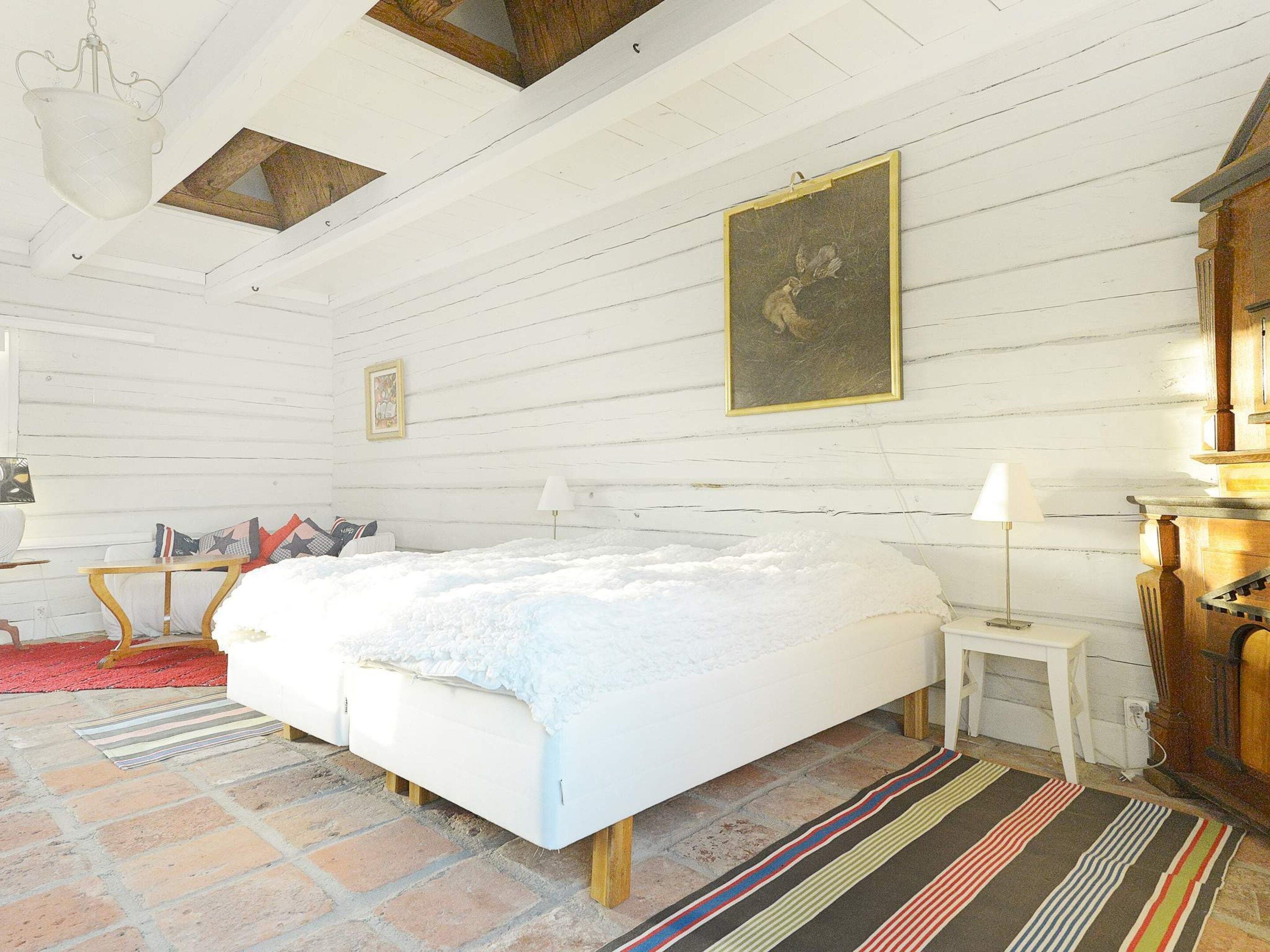 A room with a large bed, a wooden headboard, a small bedside table, a lamp, and a painting on the wall.