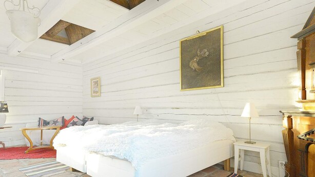 A room with a large bed, a wooden headboard, a small bedside table, a lamp, and a painting on the wall.