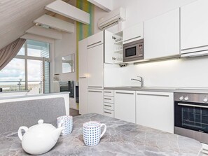 A modern kitchen with white cabinets, a built-in microwave, and a large oven. There are two patterned mugs on the marble countertop. - Holiday Home in Wendtorf (Wendtorf)