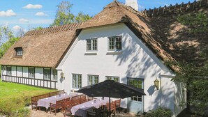 Ein traditionelles weißes Haus mit einem Strohdach, einer Steinterrasse mit Holzmöbeln und einem Garten.