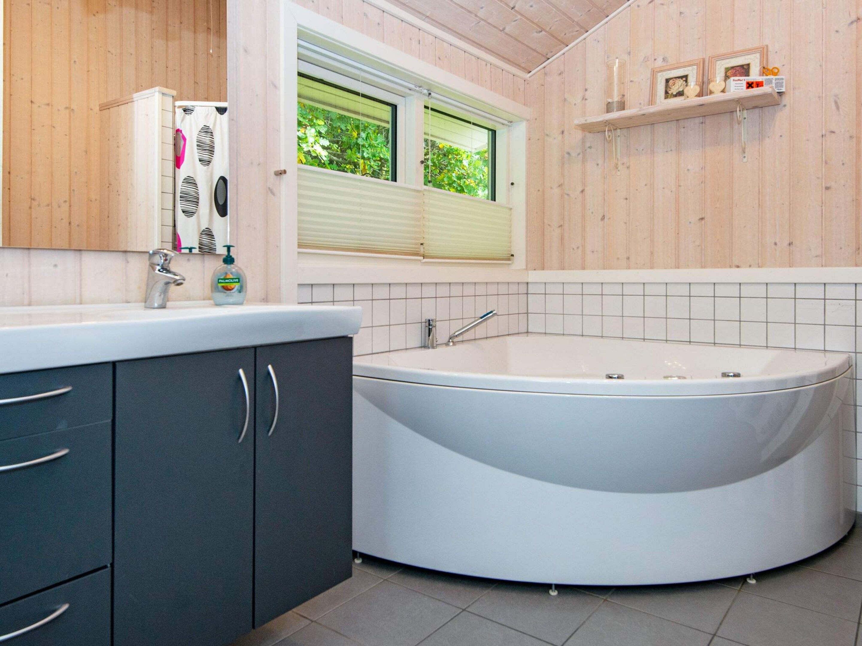 A bathroom with a freestanding bathtub, a vanity with dark cabinets, a window with blinds, and a shelf with decorative items.