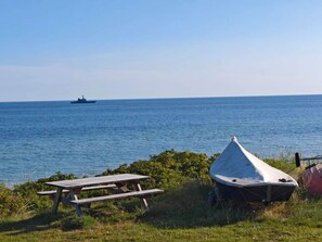 Uma mesa de piquenique e uma tenda à beira de um corpo d'água, com um navio ao longe.
