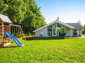 A house with a patio, a swing set, and a slide in a grassy yard. - 4 Star Holiday Home in Glesborg (Glesborg)