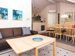 Una habitación acogedora con sofá, una mesa de comedor con sillas, una zona de cocina y obras de arte en las paredes.