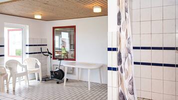 A room with a ceiling fan, a window with a view, a white table, and a shower area.