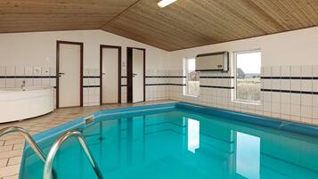 A swimming pool with a wooden ceiling and tiled walls, a bathtub, and a window with a view.
