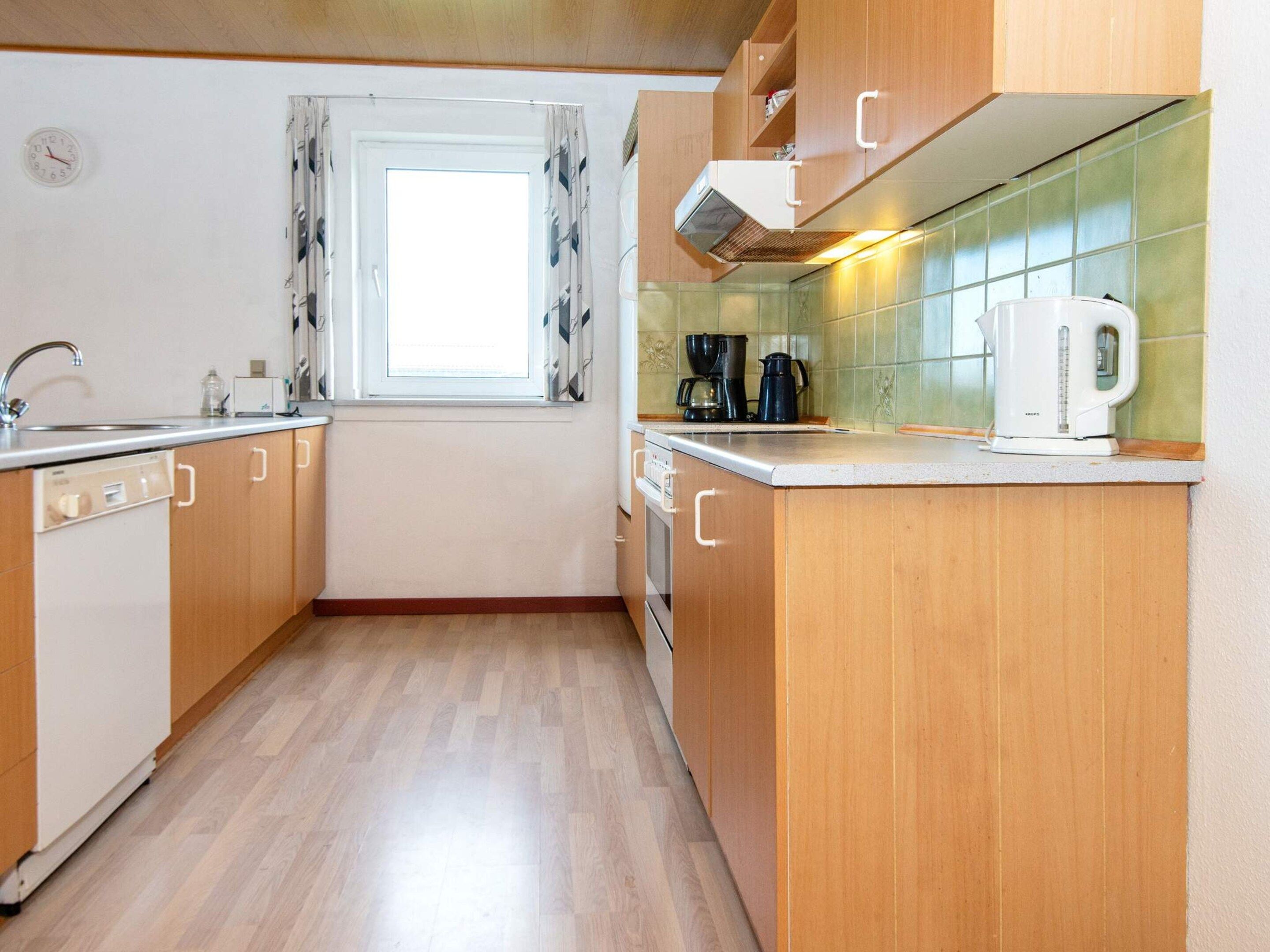 A kitchen with wooden cabinets, a window with curtains, a sink, a coffee maker, and a kettle.