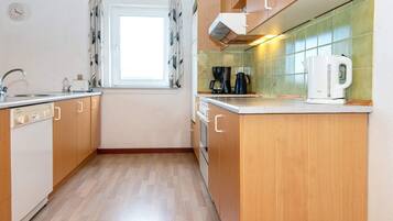 A kitchen with wooden cabinets, a window with curtains, a sink, a coffee maker, and a kettle.